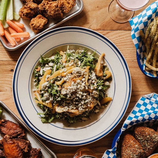 Overhead view of a salad with blue cheese, fried chicken, fries, and wings on a wooden table.