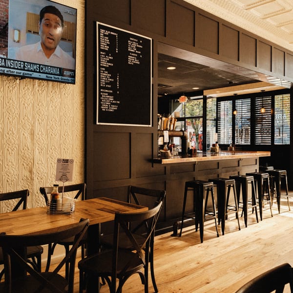 Interior of Elsie Lane Huntington, featuring a bar with stools, dining tables, and a menu board.