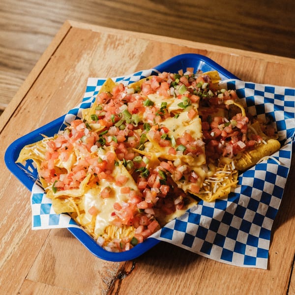 Elsie Lane Huntington's nachos, topped with melted cheese, diced tomatoes, and green onions in a blue basket.