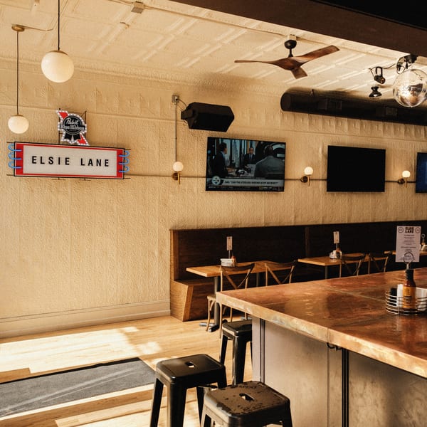 Elsie Lane restaurant interior with a neon sign, bar, booths, and TVs showing sports.
