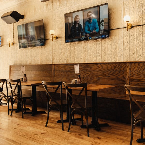 Elsie Lane Huntington dining area with wooden tables, chairs, and two wall-mounted TVs showing a baseball game.
