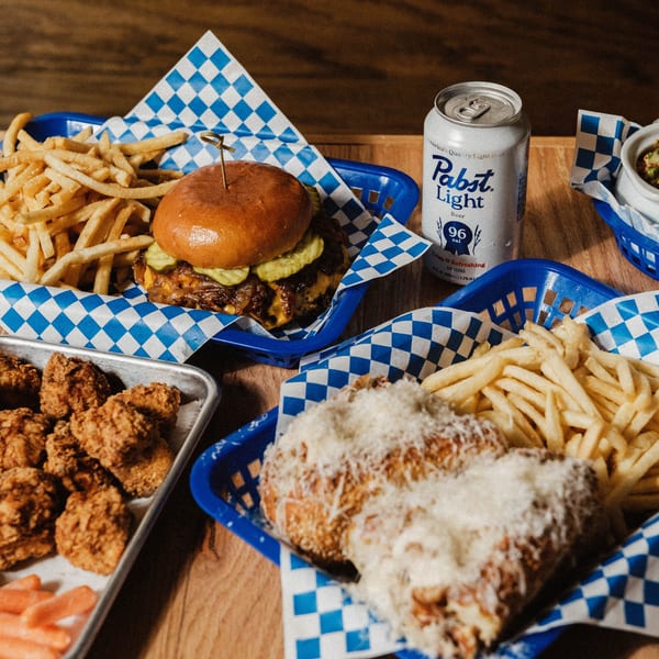 Elsie Lane Huntington's burger, fries, chicken wings, and a Pabst Light beer on a wooden table.