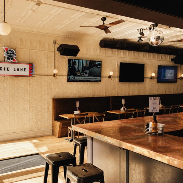 Interior of Elsie Lane Huntington, featuring a bar, dining tables, TVs, and a disco ball.