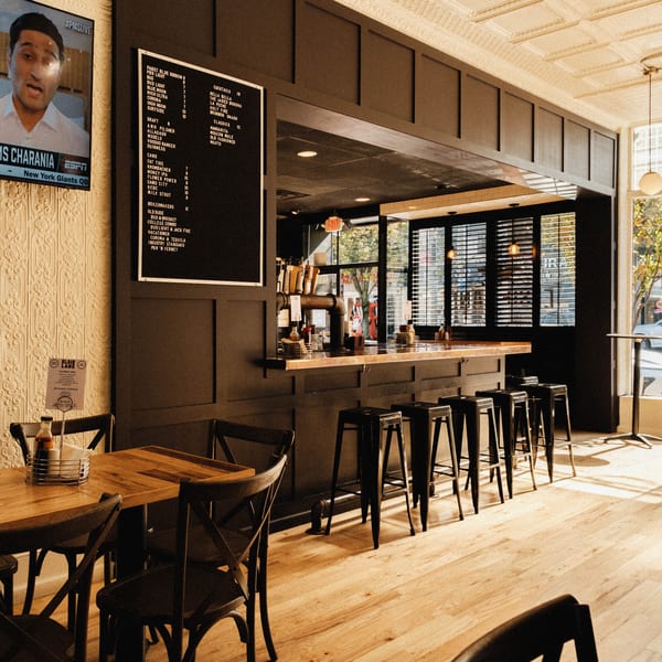 Elsie Lane Huntington's bar area with a menu board, bar stools, and wooden tables.