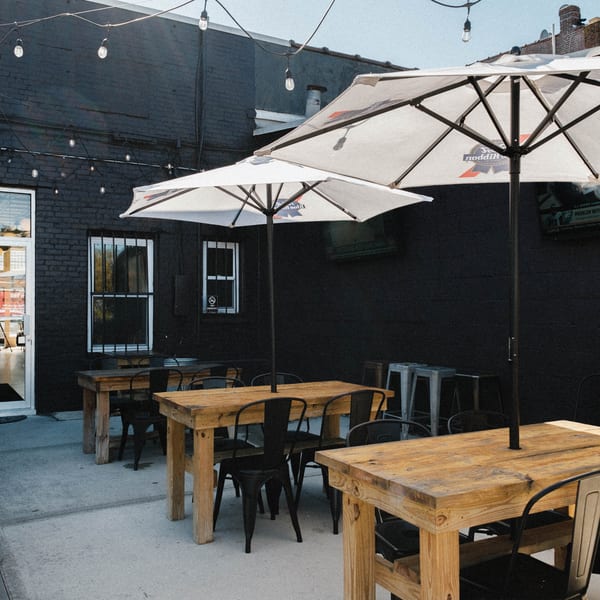 Elsie Lane Huntington's outdoor patio with wooden tables, black chairs, and white umbrellas under string lights.