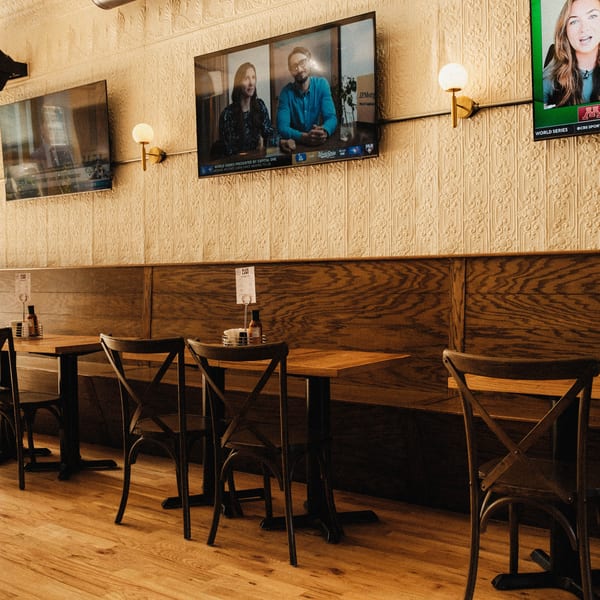 Elsie Lane Huntington's dining area with wooden tables, chairs, and TVs showing sports on a textured wall.
